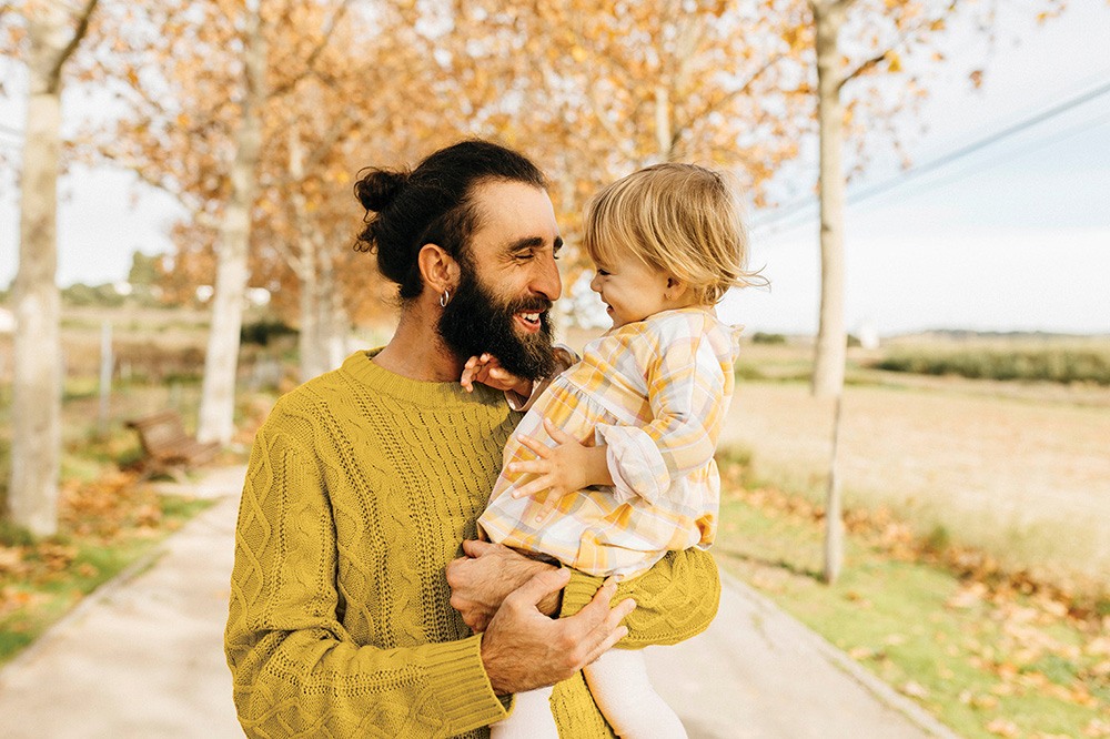 A smiling father carrying his daughter on a morning day in the park in autumn.