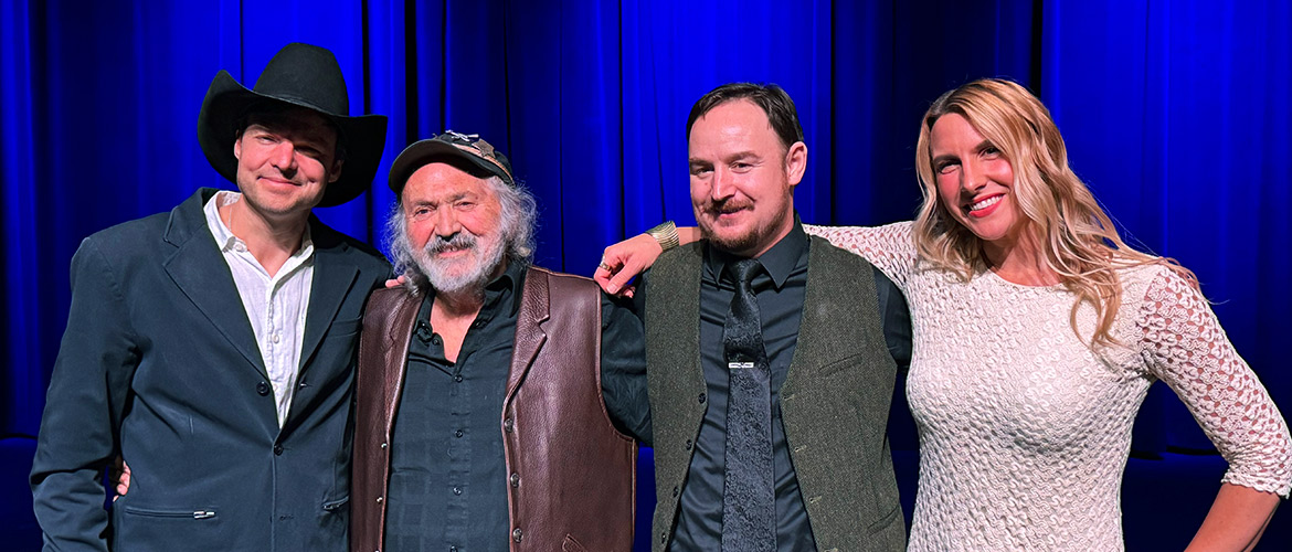 Three male and one female country music articsts pose together on stage. 